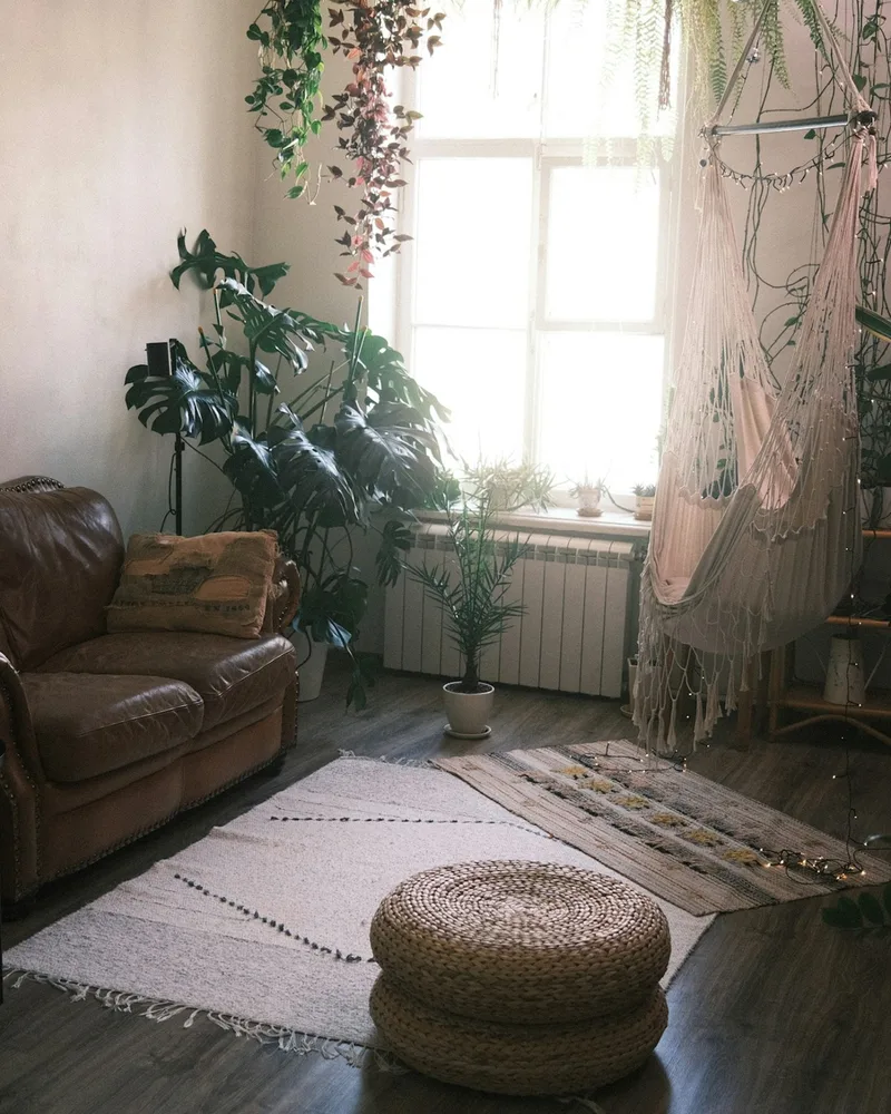 A sofa, a woven pouf and large plants by a bright window, original photo